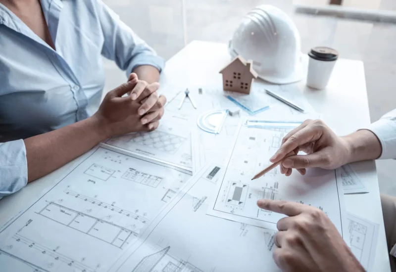 Architects or engineering team consulting and analyzing working on objects tools and construction drawings inspection planning new architectural project on blueprint and model house in modern office.